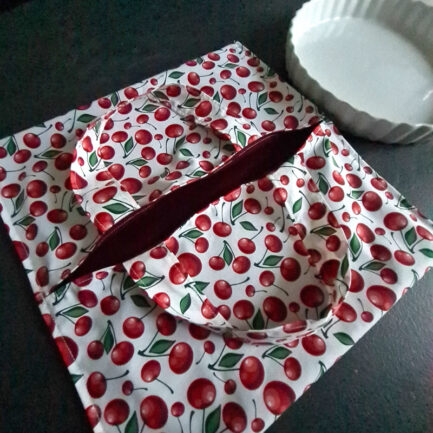 Un sac à tarte blanc avec des cerises rouge posé sur une table de cuisine